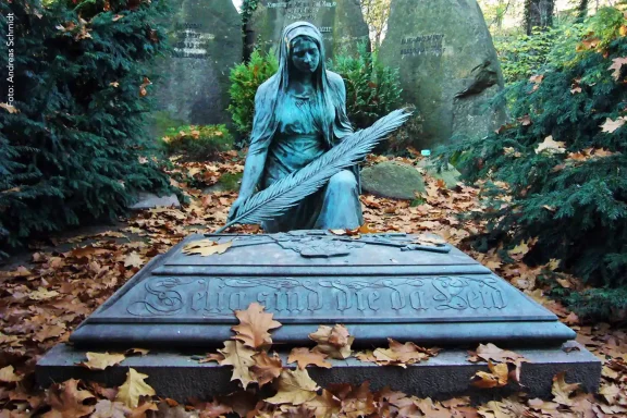 Grabfigur aus verwitterter Bronze im herbstlichen Laub.