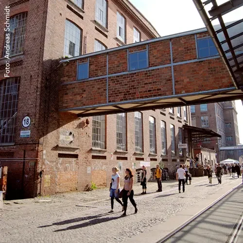Die historischen Werksgebäude der Baumwollspinnerei mit Passanten.