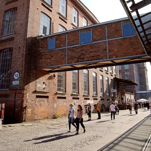 Historische Backsteingebäude der Spinnerei mit Besuchern im Abendlicht.